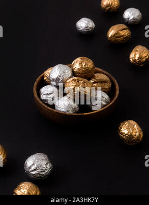 Painted golden and silver walnuts on wooden plate on black background Stock Photo