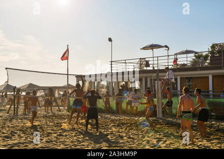 Backlight view of boys playing beach volleyball on the sandy beach of Lido di Camaiore in a sunny mid-August day, Versilia, Tuscany, Italy Stock Photo