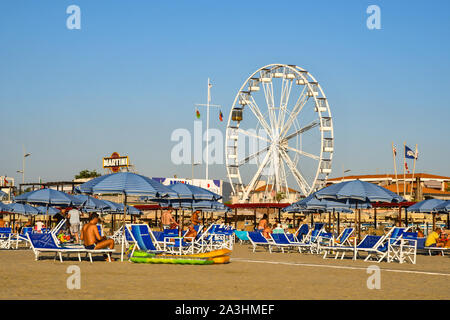 Scenic view of the sandy beach of Lido di Camaiore with people on vacation relaxing under sun umbrellas and a panoramic wheel,  Tuscany, Italy Stock Photo