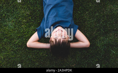 Overhead shot of boy laying on grass with arms behind head laughing. Stock Photo