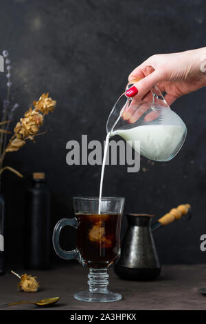 Woman's hand pouring milk in to coffee, hot drink, trendy dark style image. Frozen motion. Stock Photo