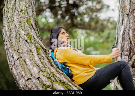 young woman hiking and standing near a tree trunk tired Stock Photo