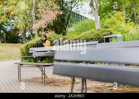 young woman siting on a bench with benchs in front Stock Photo