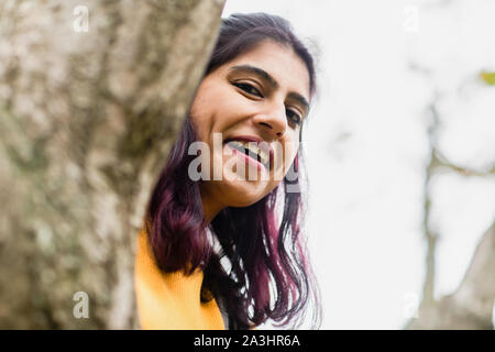 young woman looking behind a tree Stock Photo