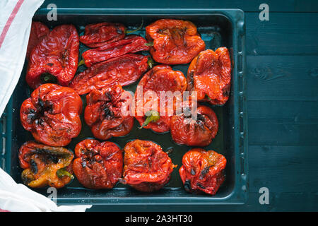 Roasted red peppers in baking tray on black wooden background. Stock Photo