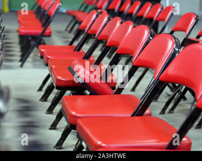Rows of red folding chairs with one raised seat. Stock Photo