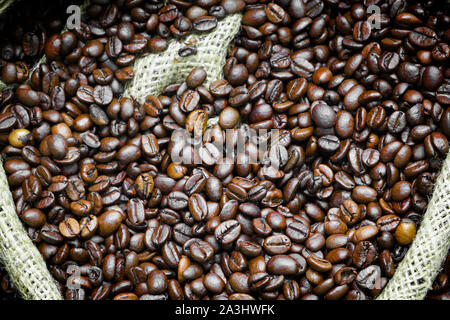 Roasted coffee beans falling in a burlap sack. Sackcloth bag with coffee beans, background. Coffee export. Stock Photo