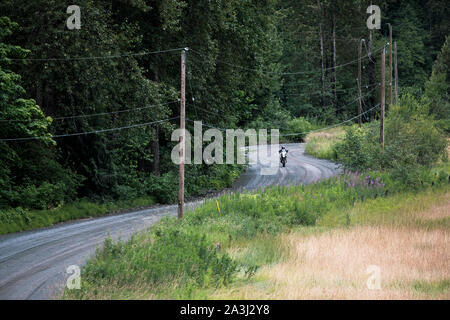 A women rides her motocycle on a gravel road in Canada. Stock Photo