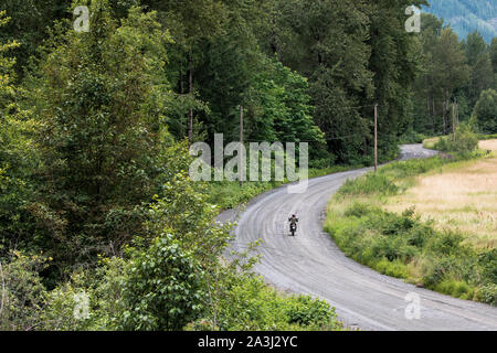 A women rides her motocycle on a gravel road in Canada. Stock Photo