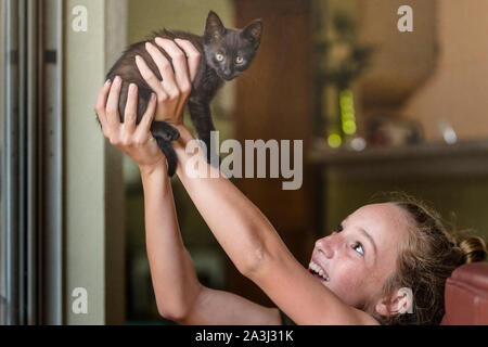 Teen girl smiles as she lifts tiny black kitten high in the air Stock Photo