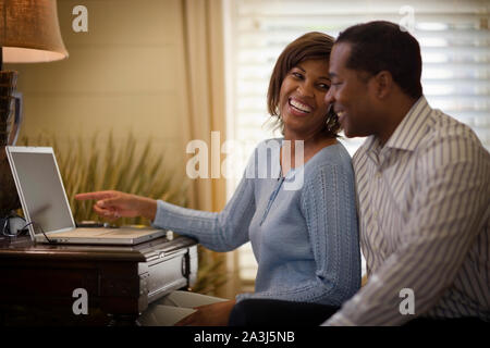 Happy mid-adult couple sitting together while using a laptop. Stock Photo
