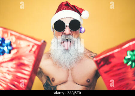 Tattooed fit santa claus doing crazy and giving christmas gifts - Trendy beard hipster senior wearing xmas clothes and holding presents Stock Photo