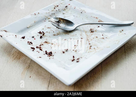 A spoon resting on an empty square plate after a chocolate dessert has been eaten in a restaurant. Stock Photo