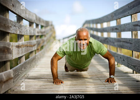 Portrait of a mature adult man doing push ups along a wooden path. Stock Photo