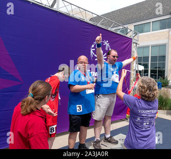 Special Olympics winner standing on top tier of podium raises hands over head with thumbs up at St Thomas University Campus. St Paul Minnesota MN USA Stock Photo