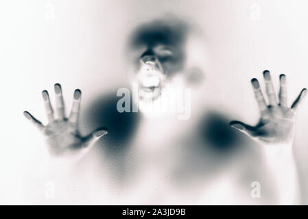 Creepy man looking behind the frosted glass and holding it with two hands.  Inverse colors version. Stock Photo