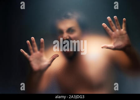 Creepy man looking behind the frosted glass and holding it with two hands. Stock Photo