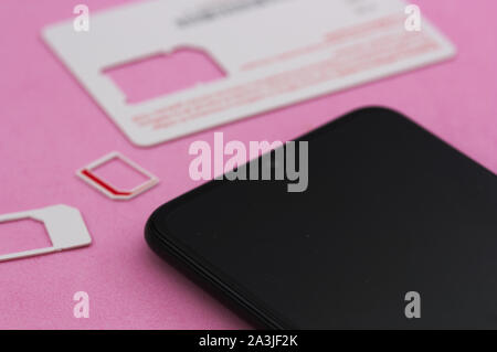 Some mobile phone cards (sim cards) next to a next-generation smart phone on a pink background. Stock Photo