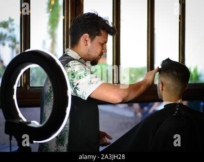 After a new haircut, barber preps a client for a shave with the help of a modern ring light at '81 Barbers in Tucson, AZ, USA Stock Photo
