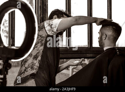 After a new haircut, barber preps a client for a shave with the help of a modern ring light at '81 Barbers in Tucson, AZ, USA Stock Photo