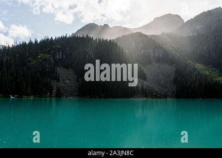 The sun shines through rain and clouds above Joffre Lake. Stock Photo