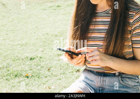 Young woman using her smartphone sitting at a park, partial view Stock Photo