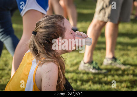 Exhausted teen girl cross country runner drinks water after race Stock Photo