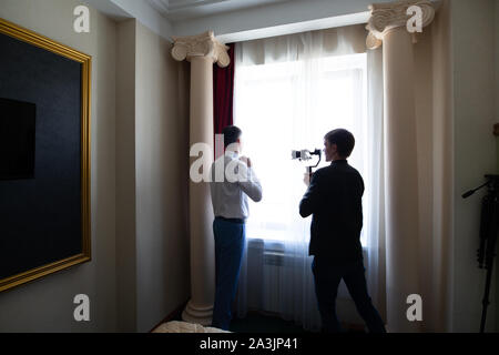 Novosibirsk, Russia - 06.15.2019: A videographer operator shoots a wedding video during the gathering and preparing the groom for a meeting with the b Stock Photo