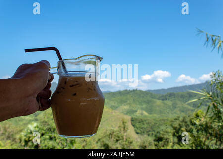 Hand holding Iced coffee in a glass jar and view  mountain. Stock Photo