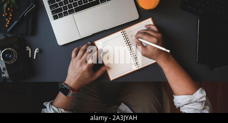 Top view of man working on his project while writing his ideas on note in dark modern workspace Stock Photo