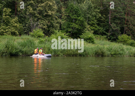 Two fishermen in life jackets with fishing rods catch fish on the river from an inflatable boat. Stock Photo