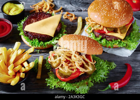 three Cheeseburgers with beef patties, cheddar cheese, crispy fried french onions, lettuce, sliced tomatoes, pickles on an old wooden table with musta Stock Photo