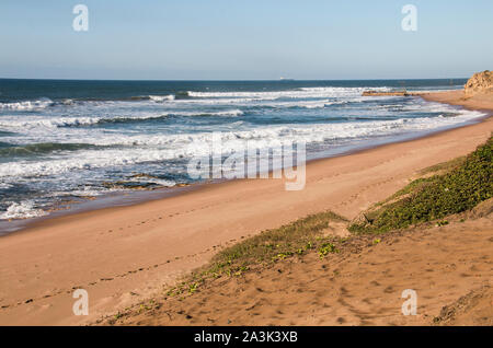Footprints in the sand with deep blue sea on an isolated coastline Stock Photo