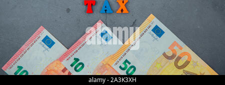 The multicolored tax word is made of wooden letters on a grey plastered wall background Stock Photo