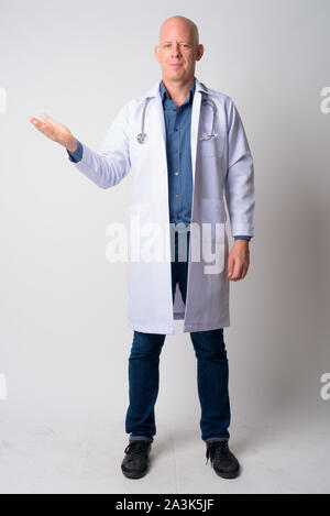 Full body shot of mature handsome bald man doctor showing something Stock Photo