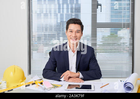 portrait of a nice smiling man, working at home on some project, he is sitting at a white table looking at camera, writing ideas with his laptop in fr Stock Photo