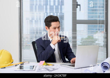 portrait of a nice smiling man, working at home on some project, he is sitting at a white table looking at camera, writing ideas with his laptop in fr Stock Photo