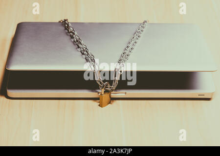Heavy chain with a padlock around a laptop on table. Stock Photo