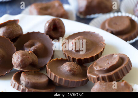 Homemade raw chocolate sweet candies with raspberries inside with droplets of water and raspberry juice on surface on white plate. Stock Photo