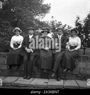 A group of 5 people sitting on a bridge before the second image peering over the bridge  from behind c1910. An early photographic attempt at humour. 1st of 2 photographs. Photo by Tony Henshaw Archive Stock Photo