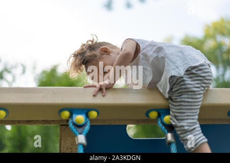 Little Caucasian girl plays on playground climbs stairs upstairs. Summer children's activity. Healthy living. Summertime. Lifestyle leisure. Childhood Stock Photo