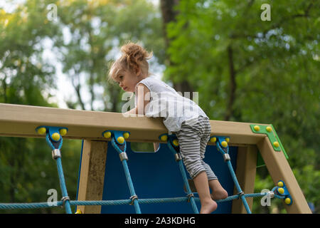 Little Caucasian girl plays on playground climbs stairs upstairs. Summer children's activity. Healthy living. Summertime. Lifestyle leisure. Childhood Stock Photo