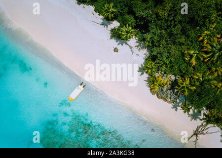 Top down aerial view of exotic tropical sandy beach with blue lagoon, palm trees and linely boat moored Stock Photo