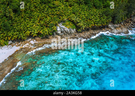 Aerial view of wild secluded lonely beach with rough granite rocks, white sand, palm trees in a jungle and turquoise water of the indian ocean at Stock Photo