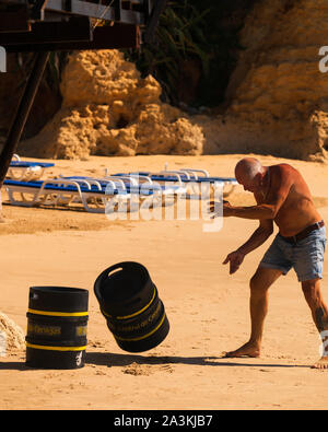 A working man deliver barrels of beer by hand to a beach restaurant on a hot summer day in Olhos D'Agua, Algarve, Portugal Stock Photo