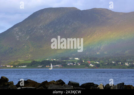Alesund fjord sea view with sailing vessel and colorful rainbow, rainbow against mountain at the fjord near Alesund in norway in early summer Stock Photo