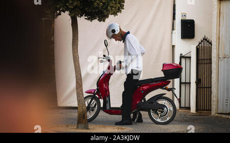 A man smokes a cigarette whilst preparing his moped for a journey in Portugal's Algarve Stock Photo