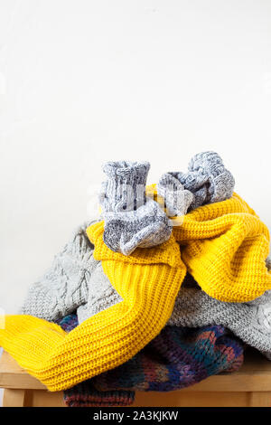 Pile colorful knitted wool clothes or sweaters on wooden table and white wall indoor close-up with copy space.Kinfolk minimal style.Donation Stock Photo