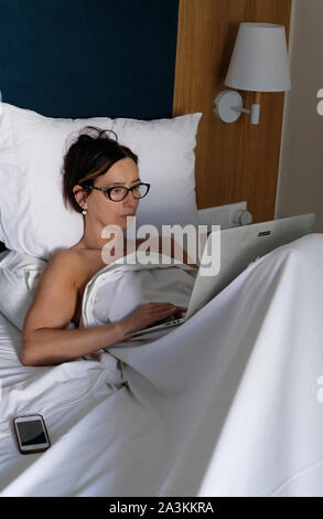 A woman working on her computer whilst in bed. Stock Photo