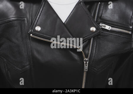 Black leather jacket with perforated elements. Metal zippers, clasps and buttons. Classic clothes for biker. Detailed closeup view. White t-shirt. Stock Photo